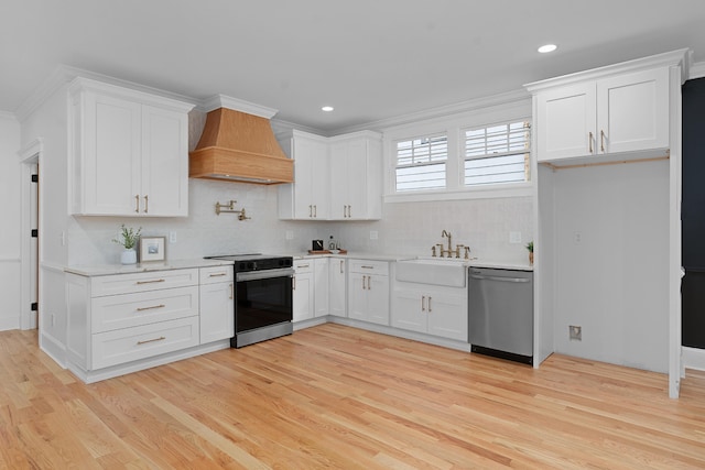 kitchen with premium range hood, appliances with stainless steel finishes, sink, light hardwood / wood-style floors, and white cabinets