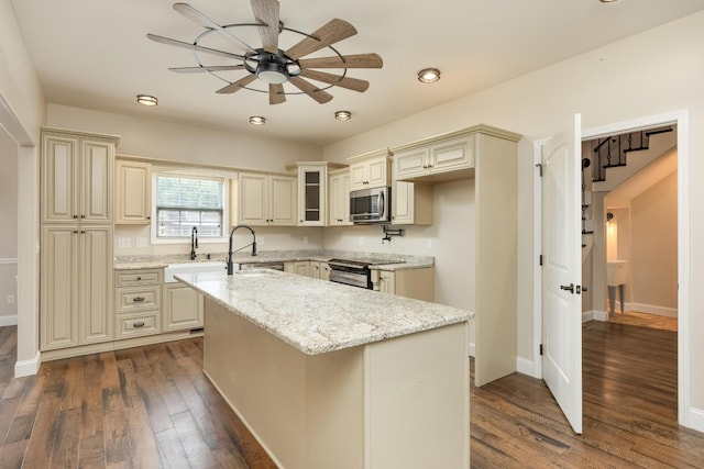 kitchen with light stone countertops, stainless steel appliances, cream cabinets, and dark hardwood / wood-style flooring