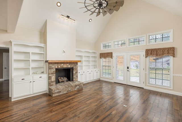 unfurnished living room with track lighting, a brick fireplace, plenty of natural light, and dark hardwood / wood-style floors