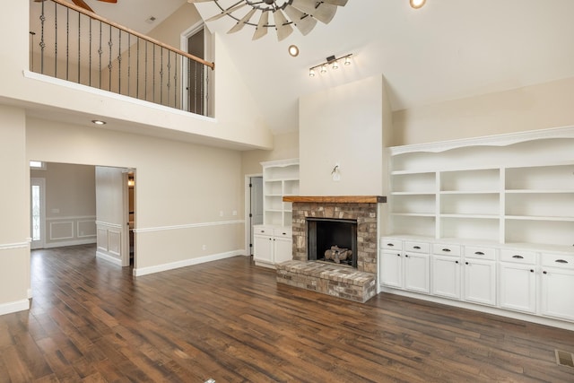 unfurnished living room with high vaulted ceiling, track lighting, dark hardwood / wood-style flooring, and a brick fireplace