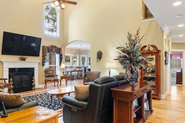 living room featuring light hardwood / wood-style floors, ornamental molding, a towering ceiling, and ceiling fan