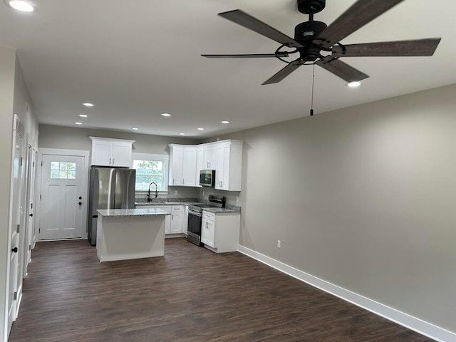 kitchen with appliances with stainless steel finishes, dark wood-type flooring, sink, white cabinets, and a kitchen island