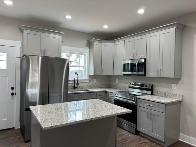 kitchen with sink, a kitchen island, appliances with stainless steel finishes, dark hardwood / wood-style floors, and light stone counters