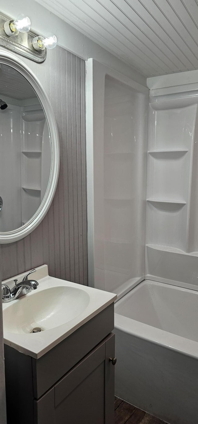 bathroom featuring wood-type flooring, wood walls, shower / bathtub combination, and vanity