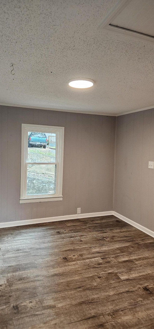 empty room featuring a textured ceiling, wooden walls, and dark wood-type flooring