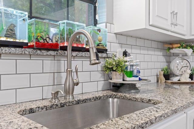 interior details featuring white cabinetry, sink, light stone counters, and tasteful backsplash