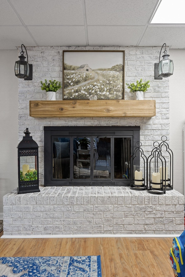 details featuring a brick fireplace, a drop ceiling, and wood-type flooring