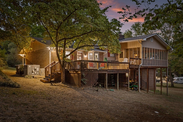 back house at dusk featuring a sunroom and a deck