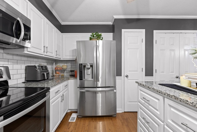 kitchen with a textured ceiling, white cabinetry, appliances with stainless steel finishes, light wood-type flooring, and crown molding