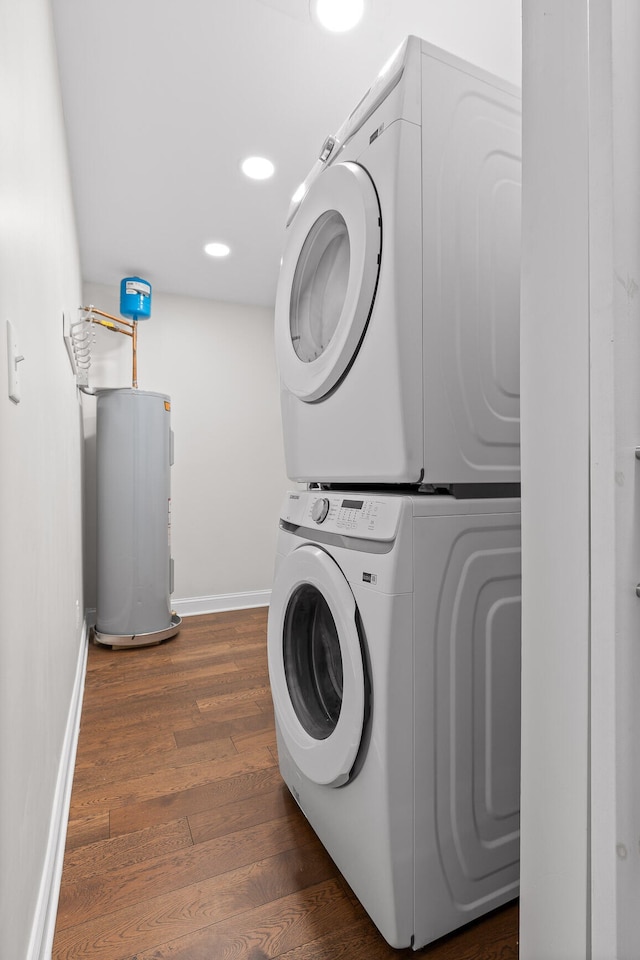 laundry area featuring electric water heater, dark wood-type flooring, and stacked washing maching and dryer