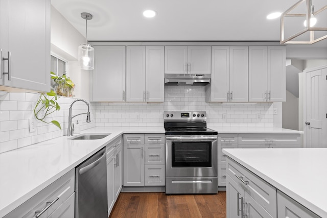 kitchen featuring tasteful backsplash, sink, stainless steel appliances, decorative light fixtures, and dark hardwood / wood-style flooring