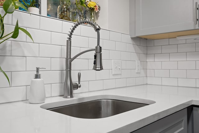 room details featuring gray cabinetry, sink, and tasteful backsplash