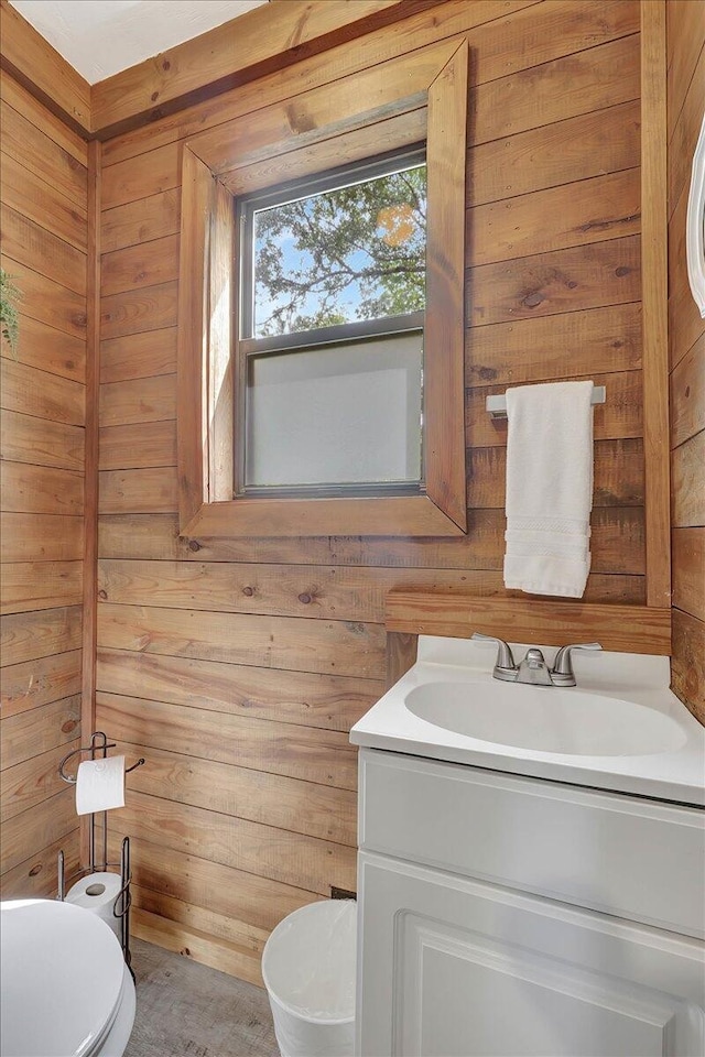 bathroom with vanity, wood walls, and toilet