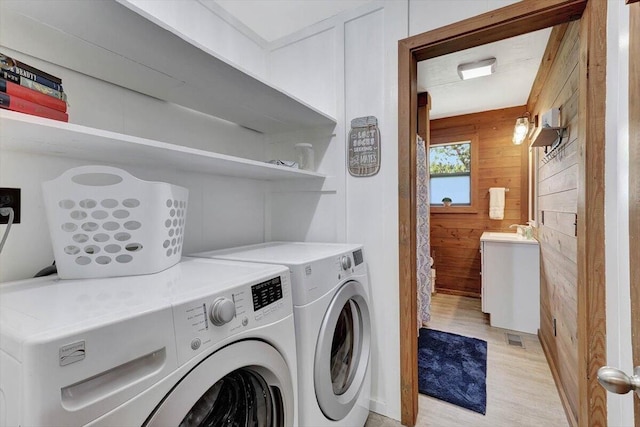 laundry room with sink, light hardwood / wood-style flooring, wood walls, and washer and dryer