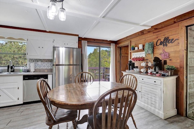 dining room with coffered ceiling, wooden walls, sink, and light hardwood / wood-style flooring