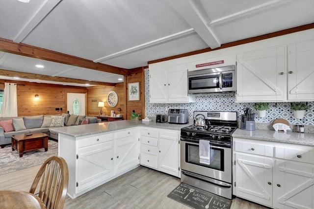 kitchen featuring beam ceiling, wood walls, kitchen peninsula, light hardwood / wood-style flooring, and appliances with stainless steel finishes