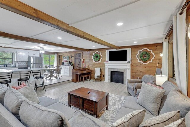 living room with wood walls, beam ceiling, a tiled fireplace, and light hardwood / wood-style flooring