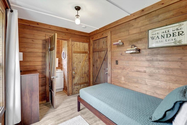 bedroom with ensuite bathroom, wooden walls, and light hardwood / wood-style floors