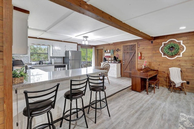 kitchen featuring white cabinets, wood walls, kitchen peninsula, light hardwood / wood-style flooring, and stainless steel appliances