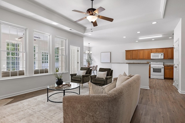 living room with ceiling fan with notable chandelier, crown molding, dark wood-type flooring, and a raised ceiling