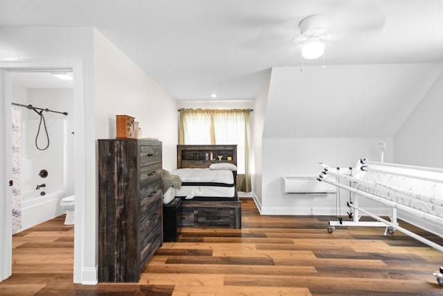 bedroom featuring hardwood / wood-style flooring, connected bathroom, an AC wall unit, and ceiling fan