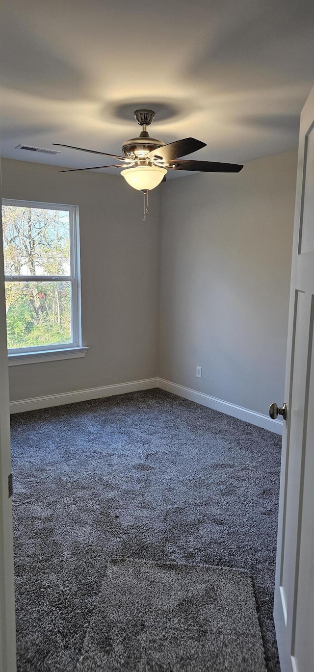 empty room featuring baseboards, visible vents, dark colored carpet, and a ceiling fan