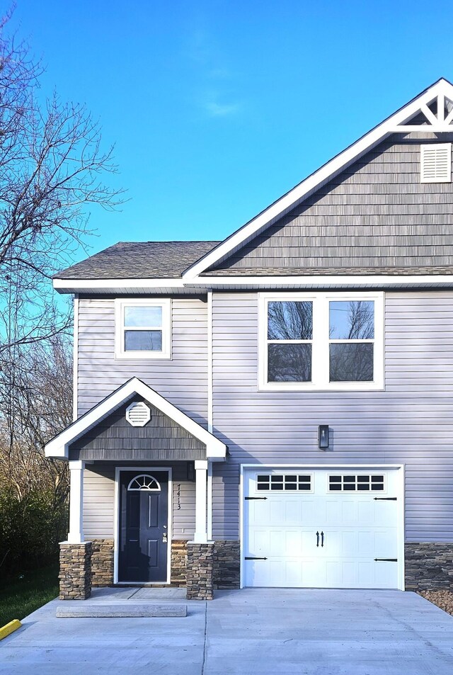 view of front facade featuring a garage, driveway, roof with shingles, and stone siding