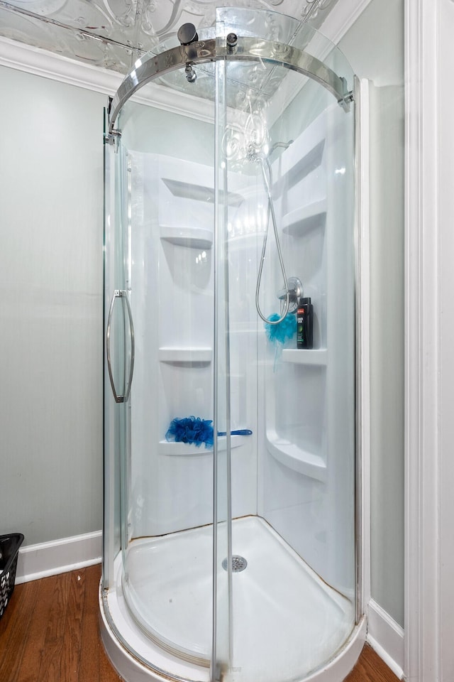 bathroom with wood-type flooring, a shower with shower door, and ornamental molding