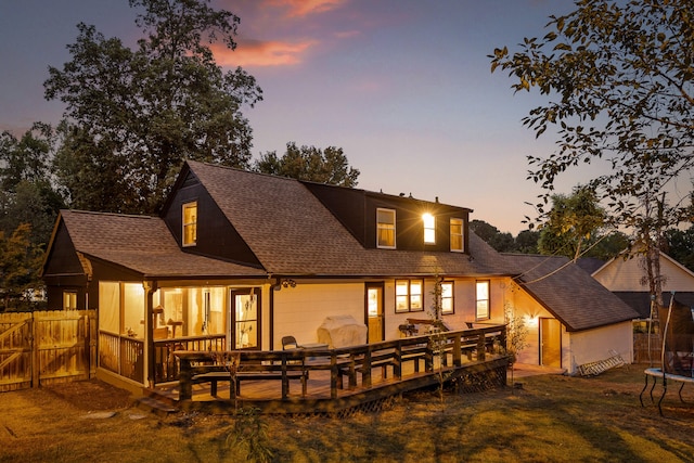 back house at dusk featuring a trampoline, a wooden deck, and a yard