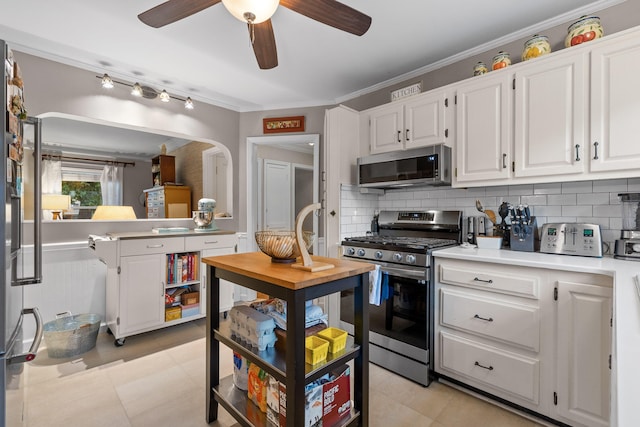 kitchen featuring white cabinets, decorative backsplash, stainless steel appliances, crown molding, and ceiling fan