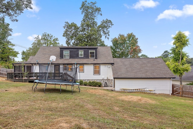 rear view of house featuring a trampoline, a lawn, and a deck