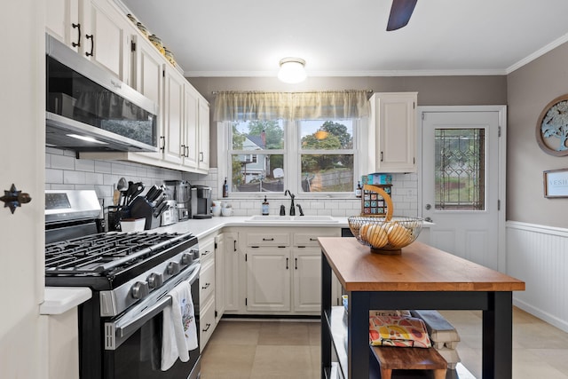 kitchen featuring appliances with stainless steel finishes, white cabinets, backsplash, crown molding, and sink