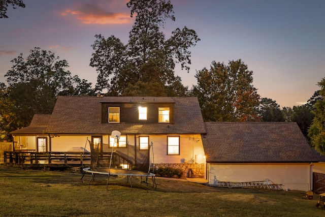 back house at dusk featuring a lawn, a trampoline, and a deck