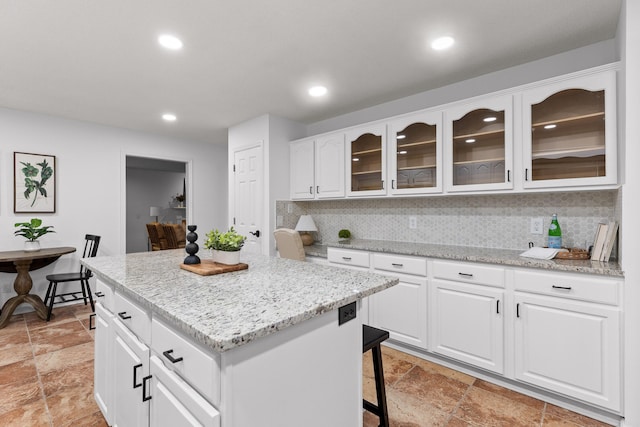 kitchen with light stone counters, white cabinets, decorative backsplash, and a kitchen island