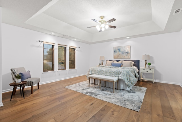 bedroom featuring a textured ceiling, a tray ceiling, hardwood / wood-style floors, and ceiling fan