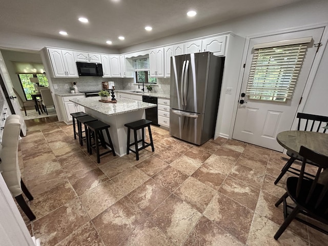 kitchen featuring a kitchen island, white cabinetry, black appliances, a breakfast bar area, and decorative backsplash