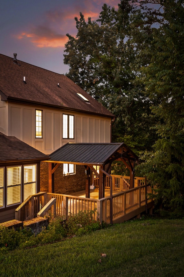 back house at dusk with a gazebo, a yard, and a wooden deck