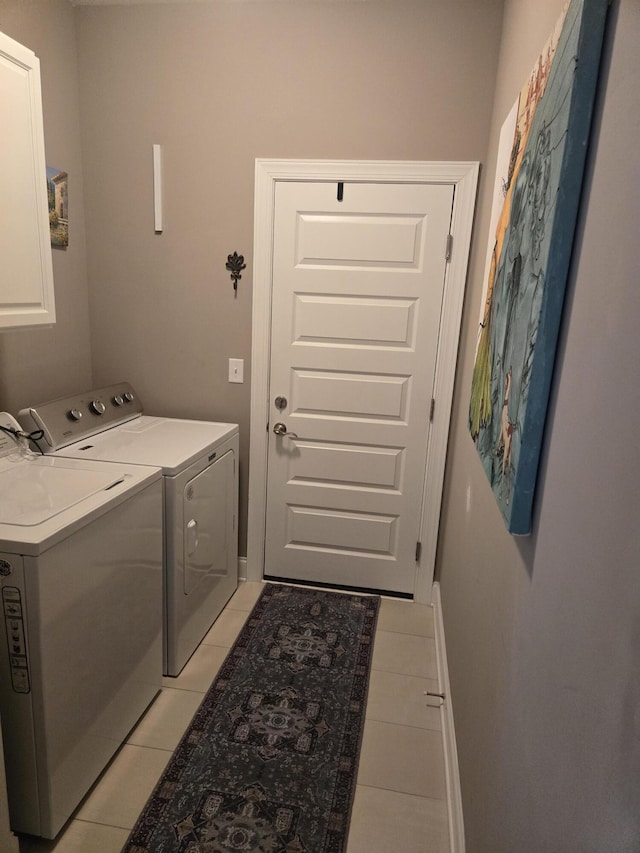 clothes washing area with washing machine and dryer, light tile patterned floors, and cabinets