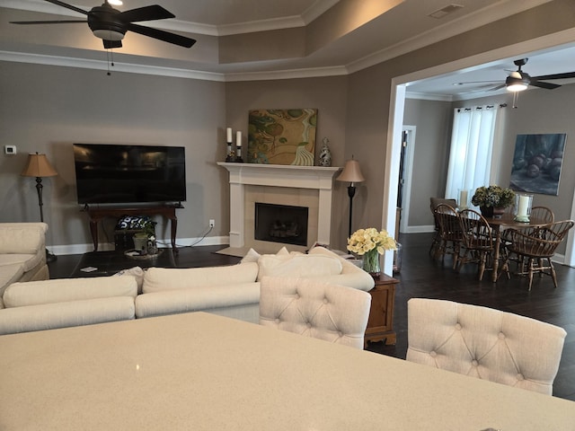 living room featuring ornamental molding, a tiled fireplace, ceiling fan, and dark hardwood / wood-style floors