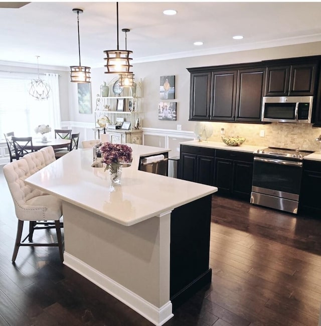 kitchen featuring dark hardwood / wood-style floors, a kitchen bar, hanging light fixtures, a kitchen island, and appliances with stainless steel finishes