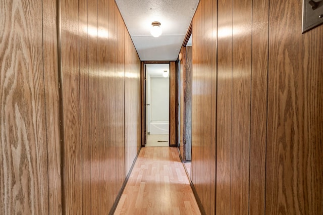 hallway featuring wooden walls, light hardwood / wood-style floors, and a textured ceiling