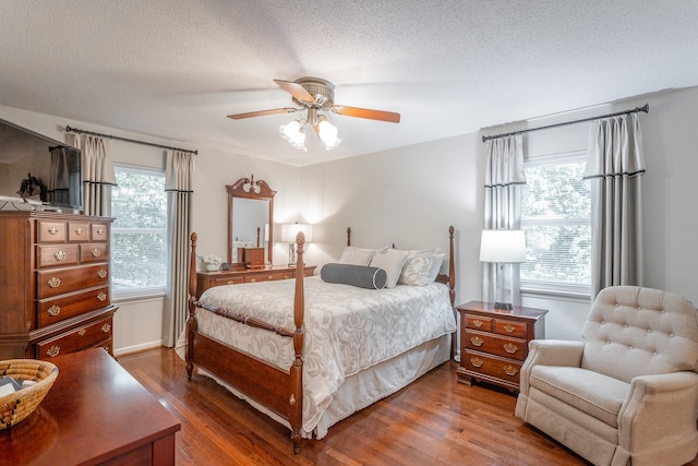 bedroom with ceiling fan, a textured ceiling, dark wood-type flooring, and multiple windows