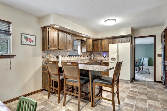 kitchen with kitchen peninsula, tasteful backsplash, a breakfast bar, a textured ceiling, and white refrigerator with ice dispenser