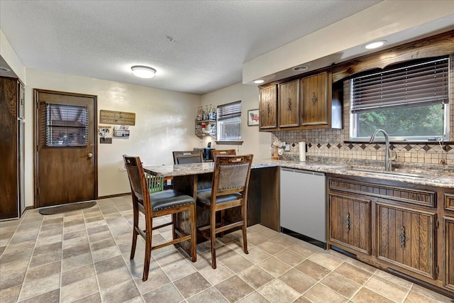 kitchen featuring light stone countertops, tasteful backsplash, a textured ceiling, sink, and dishwasher