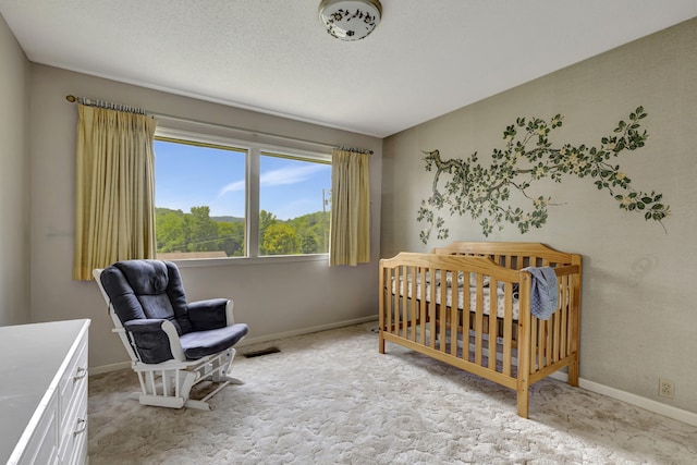 bedroom featuring light carpet, a nursery area, and a textured ceiling