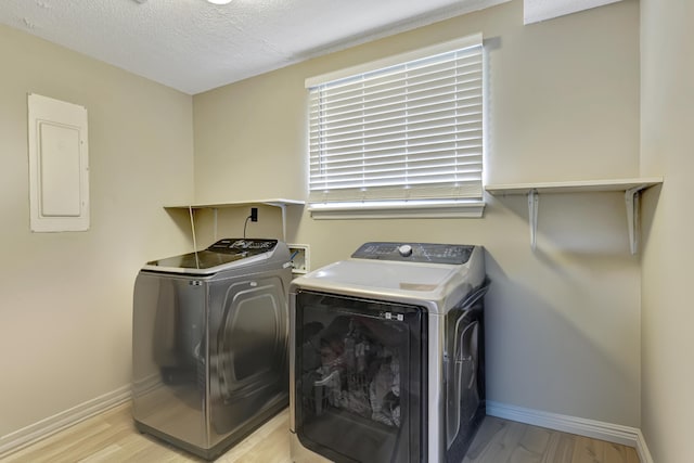 washroom featuring independent washer and dryer, a textured ceiling, electric panel, and light hardwood / wood-style flooring