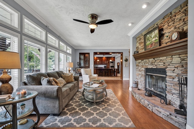 living room with a textured ceiling, dark hardwood / wood-style floors, a stone fireplace, crown molding, and ceiling fan