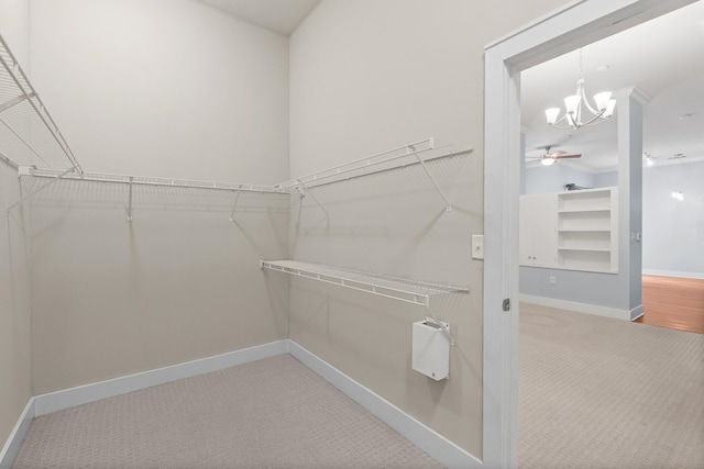 spacious closet featuring ceiling fan with notable chandelier and carpet flooring