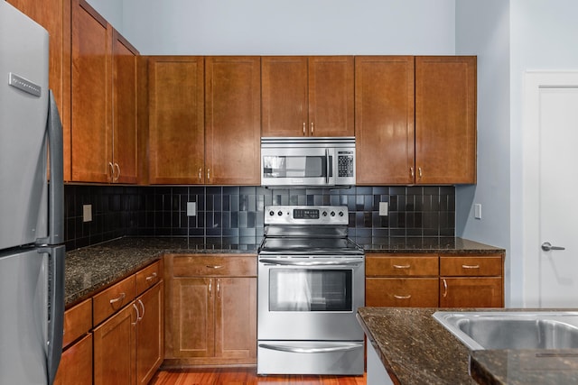 kitchen featuring appliances with stainless steel finishes, hardwood / wood-style floors, dark stone counters, and tasteful backsplash