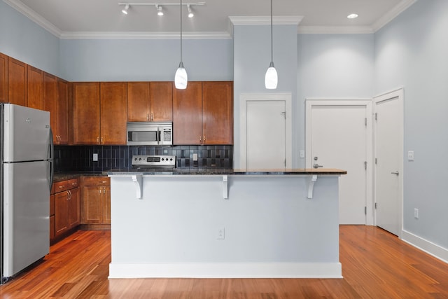 kitchen featuring appliances with stainless steel finishes, a kitchen island, pendant lighting, a kitchen bar, and hardwood / wood-style flooring